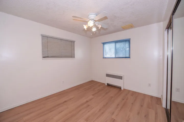 Wood-finish flooring, ceiling fan with integrated lighting, two windows, and a mirrored closet door