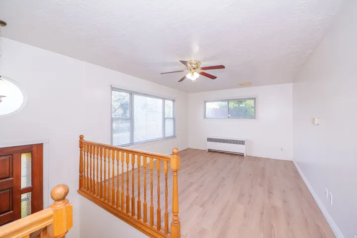 Wood-finish flooring, ceiling fan, natural wood staircase railing, rectangular windows, oval window