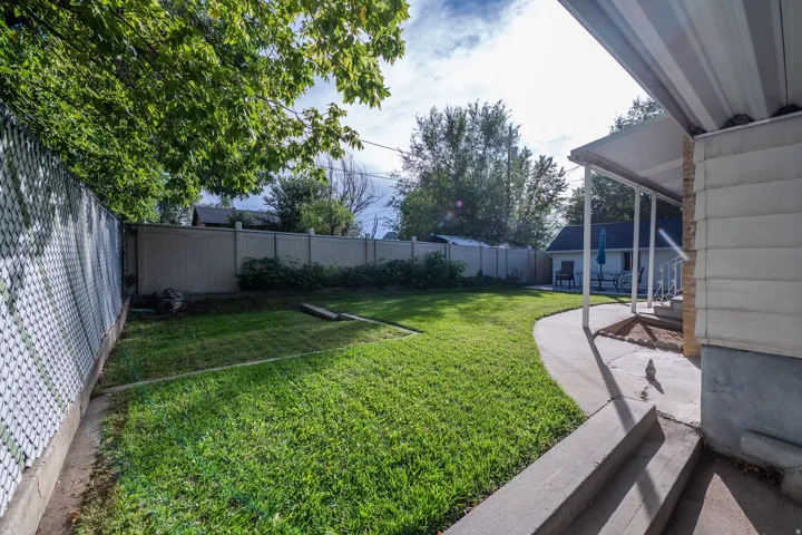 Expansive lawn area with a chain-link fence, mature trees, and a covered patio with concrete steps