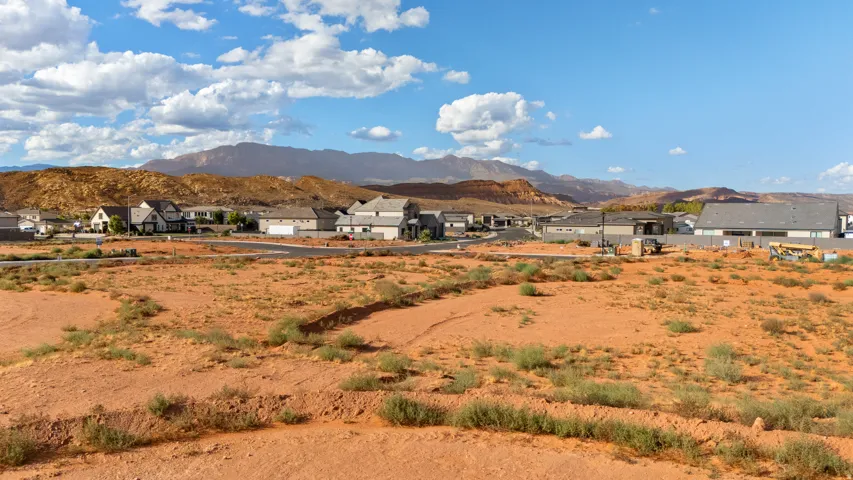 Expansive vacant land featuring a natural desert landscape, surrounded by developed residential properties, with distant mountains under a blue sky