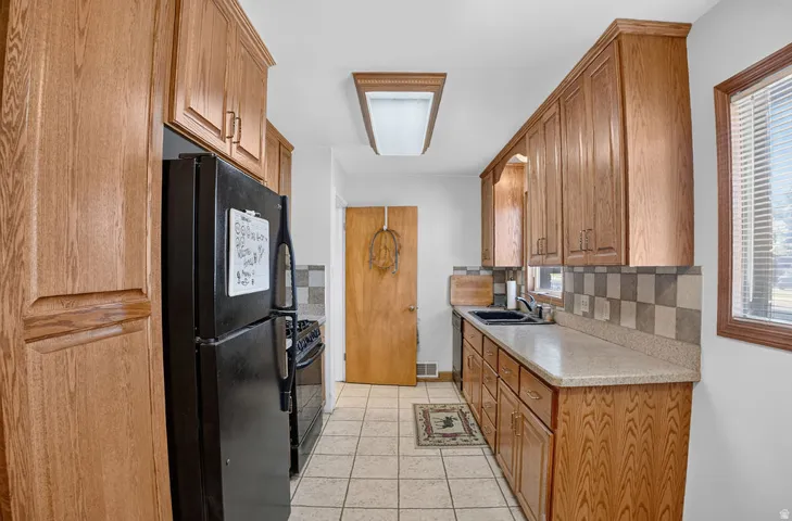 Galley kitchen featuring wood cabinetry, stone-finish countertops, checkerboard tile backsplash, and tile flooring