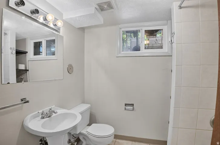 Pedestal sink with chrome faucet, toilet, and a tiled shower stall