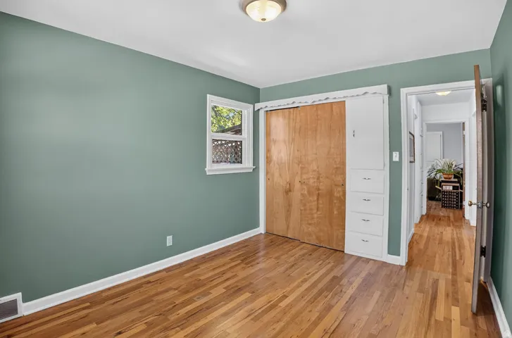 Wood-finish flooring, built-in cabinetry with drawers, ceiling-mounted light fixture, window with white trim, and a wood sliding closet door