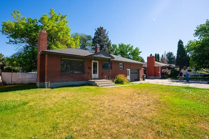 Brick exterior with an attached garage, covered entry, and mature trees