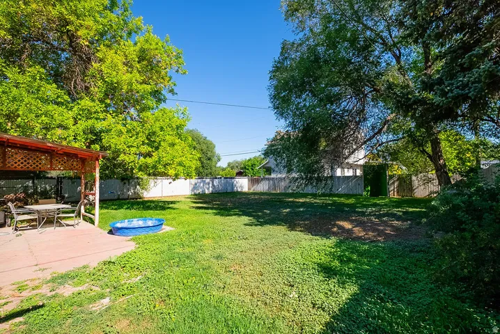 Expansive grassy yard with mature trees, a covered patio, and a privacy fence