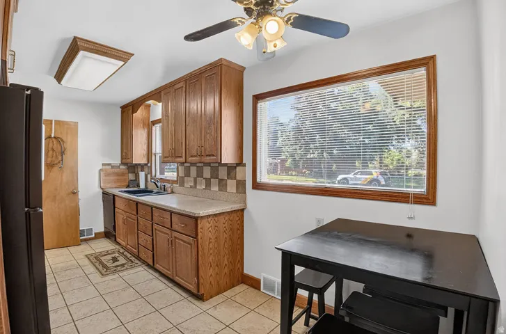 Wood-finish cabinetry, tile flooring, checkerboard tile backsplash, and a ceiling fan with light fixture
