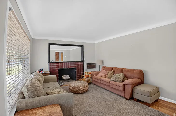 Living area featuring a tiled fireplace with a black surround, wide window with horizontal blinds, and crown molding