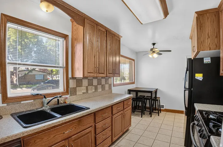 Kitchen featuring wood cabinetry, a dual basin sink, tiled flooring, and a ceiling fan with integrated lighting