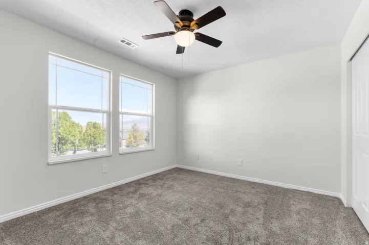 Two large windows, ceiling fan with light fixture, neutral wall color, gray carpet, and white trim
