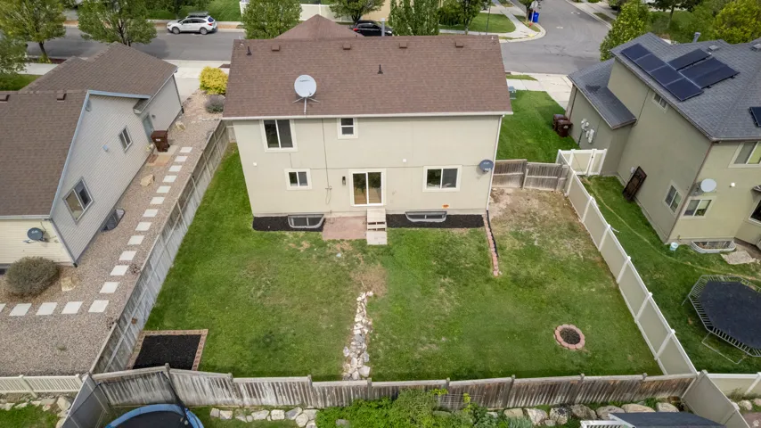 Expansive green lawn, fenced perimeter, patio with sliding glass door access, and a built-in fire pit