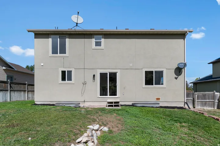 Stucco exterior with multiple windows, sliding glass door, and a grassy outdoor area
