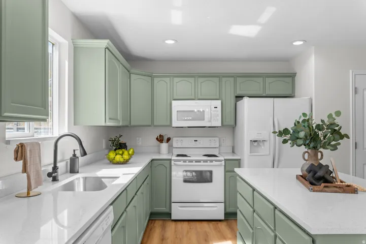 Kitchen featuring light green cabinetry, white countertops, stainless steel sink, white appliances, and wood-finish flooring
