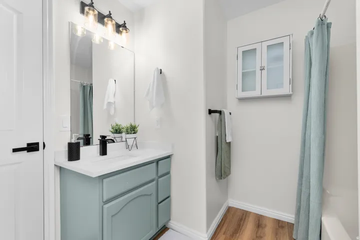 Light-colored vanity with a white countertop and rectangular sink, wood-finish flooring, and wall-mounted white storage cabinet