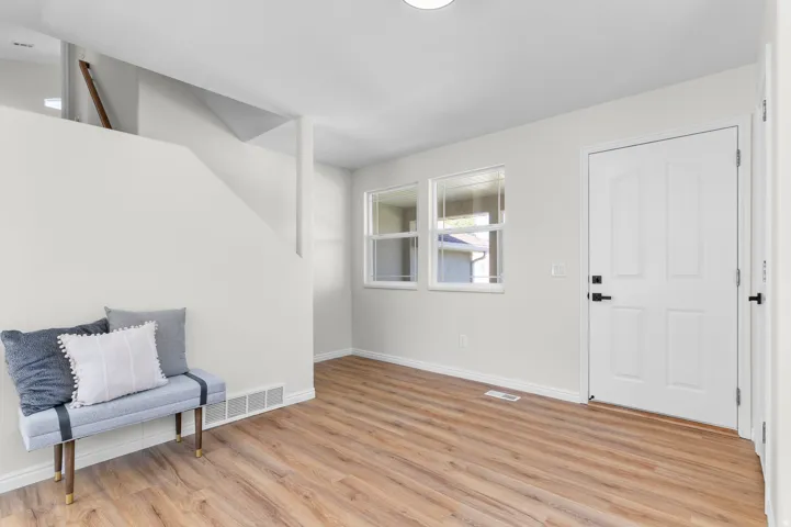 Wood-finish flooring throughout, white paneled door with black hardware, and double windows with white trim