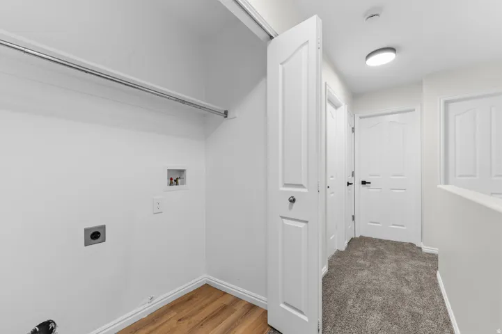 Laundry area with wood-finish flooring, white walls, and a hanging rod
