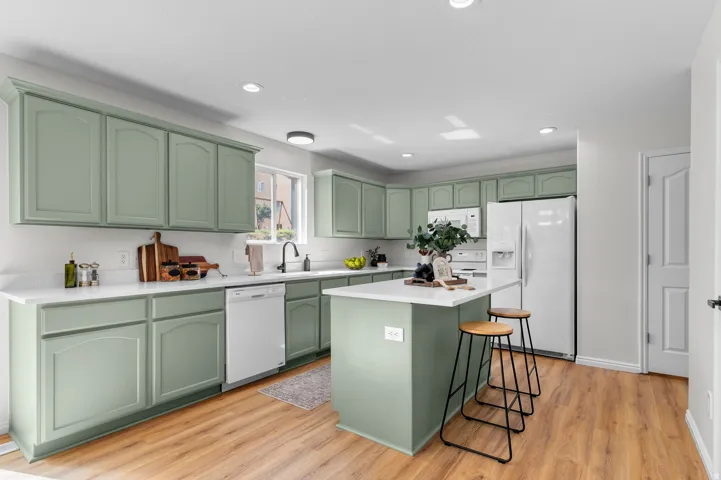 Kitchen featuring light green cabinetry, white countertops, wood-finish flooring, a kitchen island, and white appliances