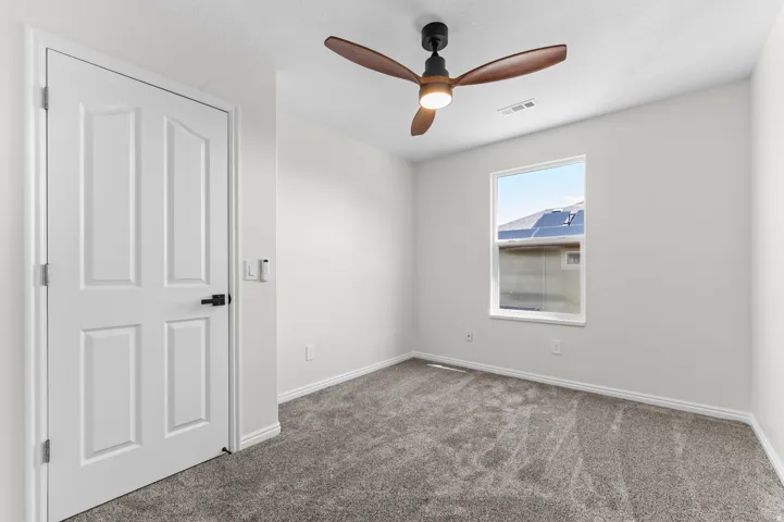 Carpeted flooring with light-toned walls, a paneled door with black hardware, a window, and a ceiling fan with integrated lighting