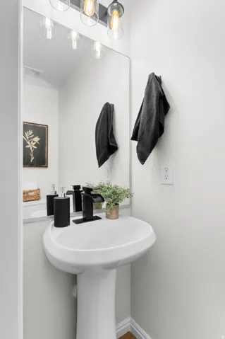 Pedestal sink with a black waterfall faucet, rectangular wall mirror, and a three-light vanity fixture