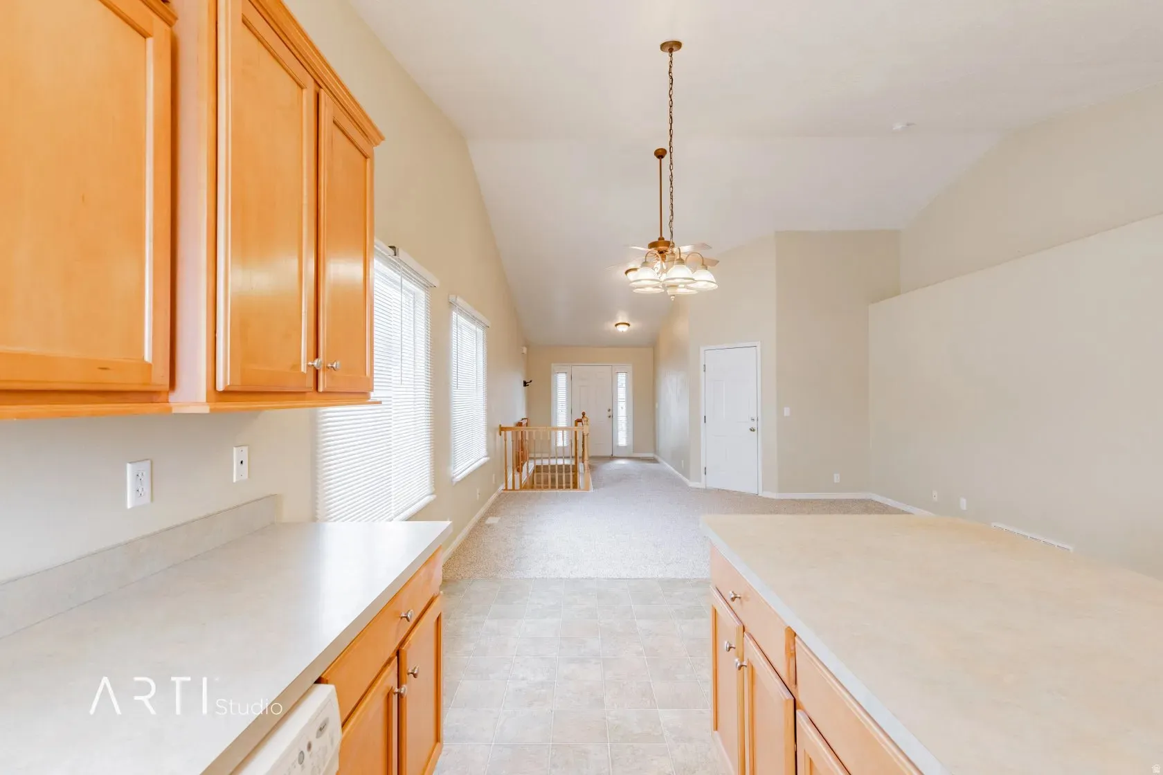 Vaulted ceiling, wood-finish cabinetry, neutral countertops, and a modern chandelier