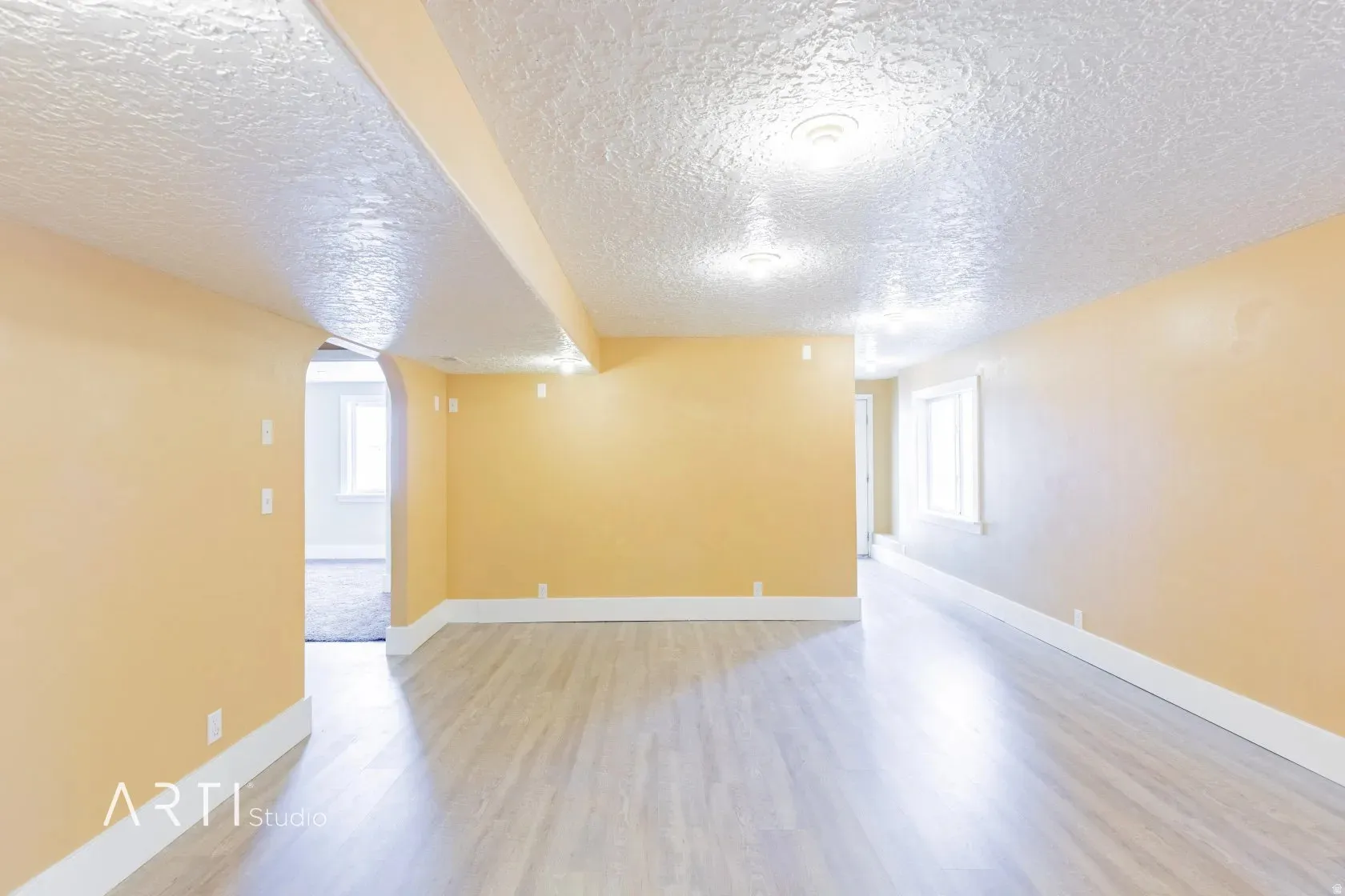 Recessed lighting illuminates the wood-finish flooring in this expansive space, featuring a window and an arched doorway