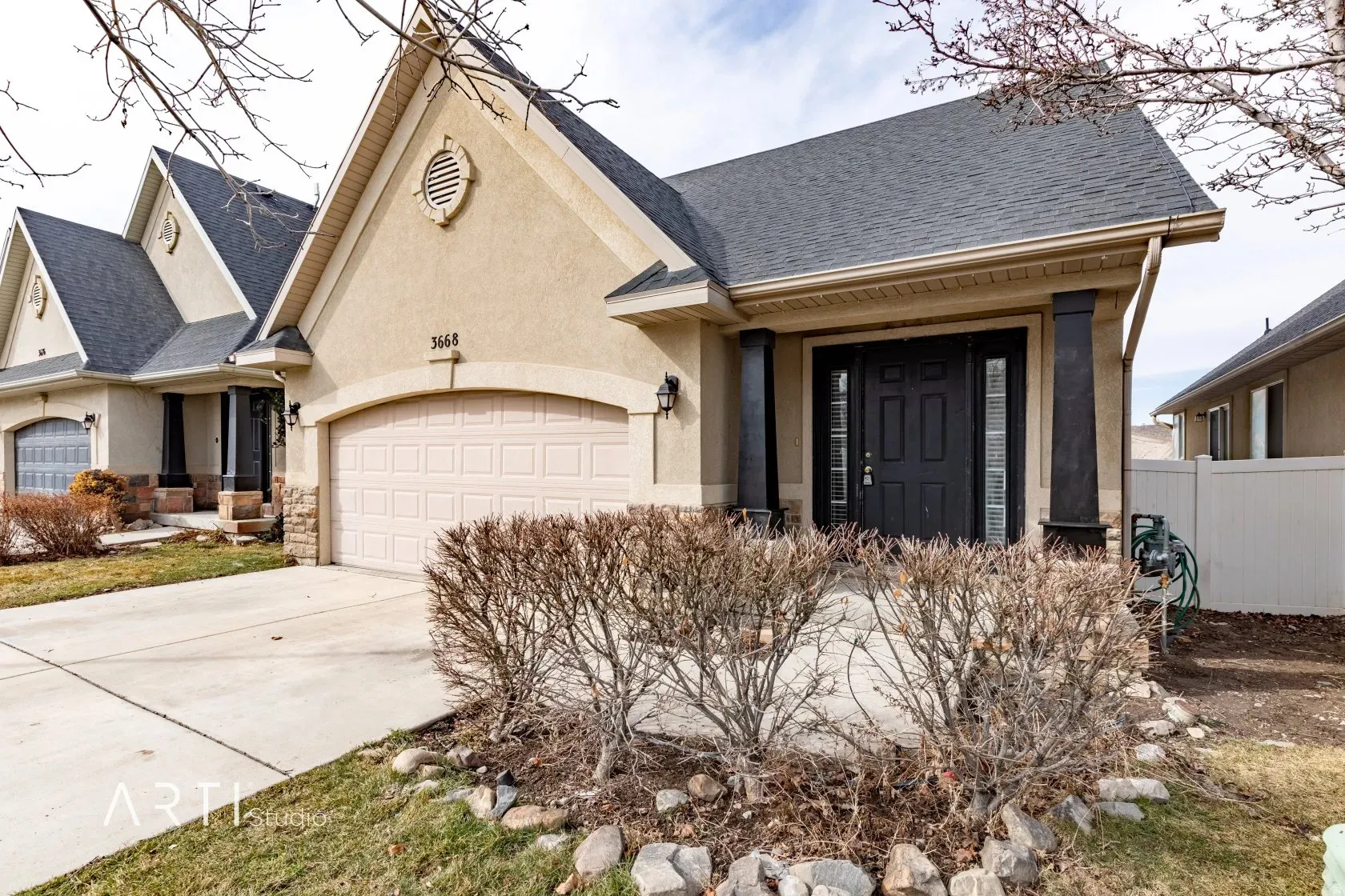 Stucco exterior with a dark shingle roof, arched garage door, and a covered entry featuring dark columns