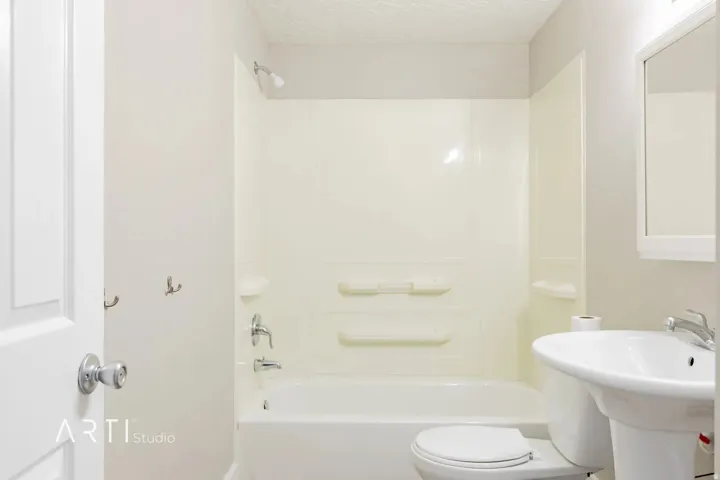 Bathtub with integrated shower, pedestal sink, wall-mounted mirror, and wall-mounted hooks