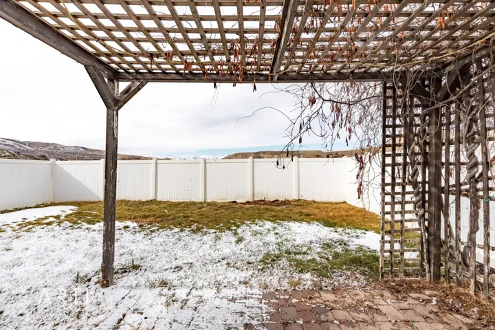 Paved patio area with a wooden pergola structure, featuring a white privacy fence and an expanse of ground cover