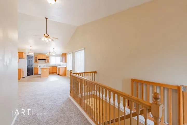 Vaulted ceiling with a ceiling fan, light wood cabinetry, white appliances, and a light-toned carpet