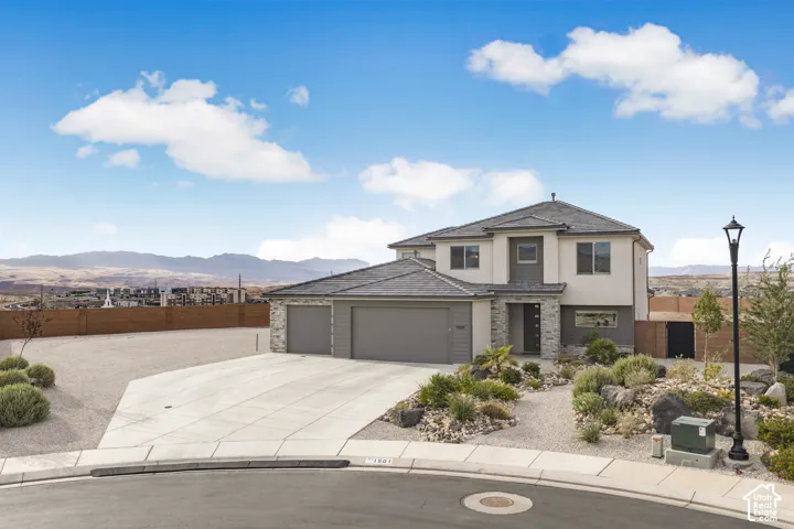 Two-story exterior featuring a stone facade, concrete tile roofing, three-car garage, and xeriscaped front yard with rock landscaping and mountain scenery