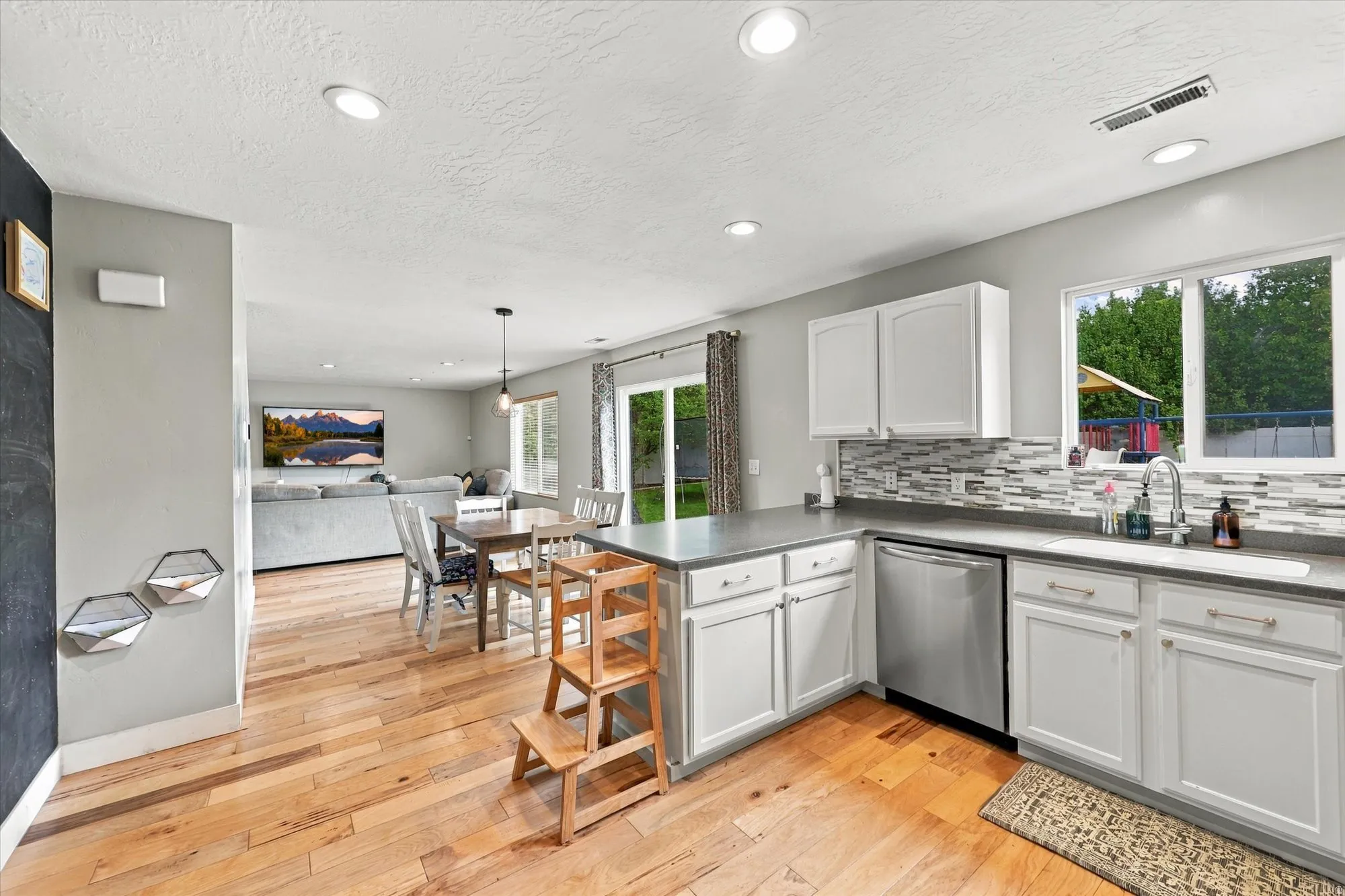 Kitchen featuring white cabinetry, stainless steel appliances, a multi-tone tile backsplash, and wood-finish flooring