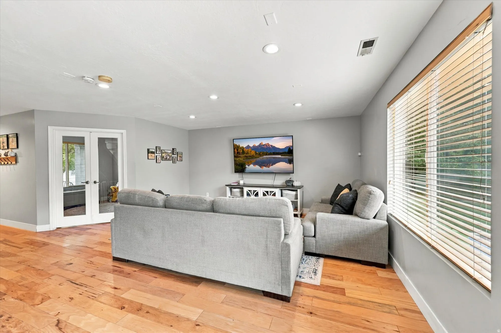 Wood-finish flooring, recessed lighting, white trim, dual-pane windows with blinds, and double French doors with clear glass panels
