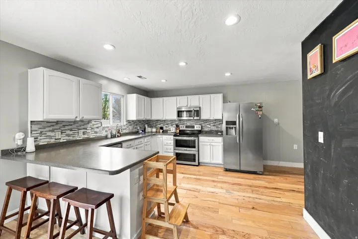 Kitchen featuring white cabinetry, stainless steel appliances, a mosaic tile backsplash, and wood-finish flooring