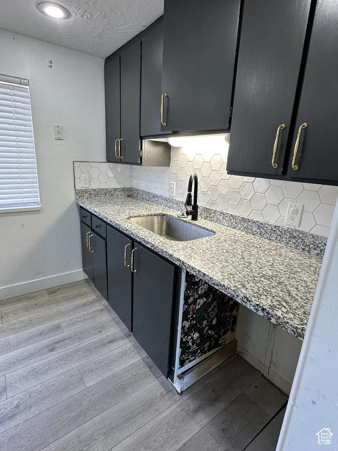 Kitchen featuring dark cabinetry with gold-toned hardware, speckled countertops, a hexagon tile backsplash, and a stainless steel sink with a black faucet