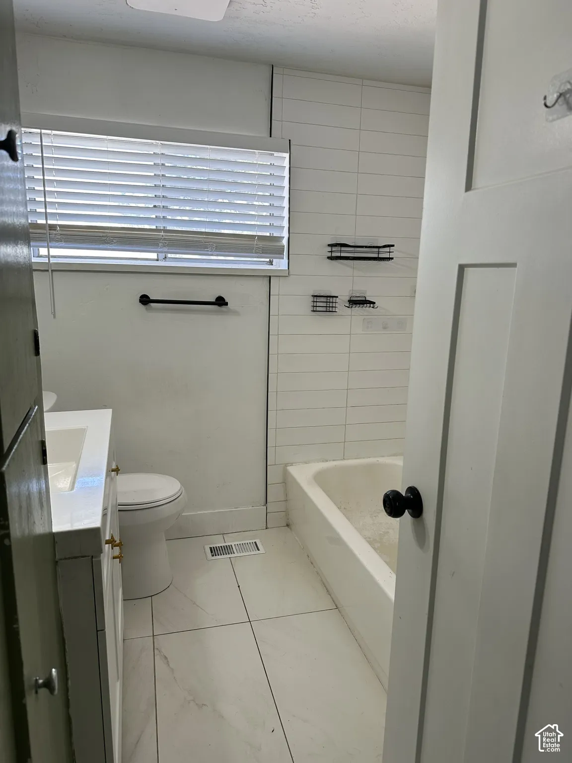 White tile flooring, white vanity with gold-tone hardware, rectangular undermount sink, white bathtub, and horizontal wall tiling