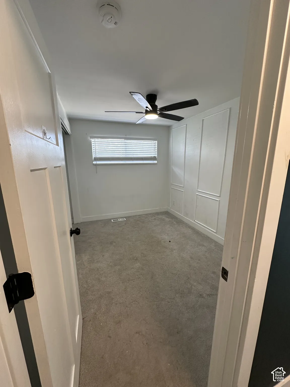 Wall paneling, ceiling fan with integrated lighting, window with horizontal blinds, and neutral-toned carpeting