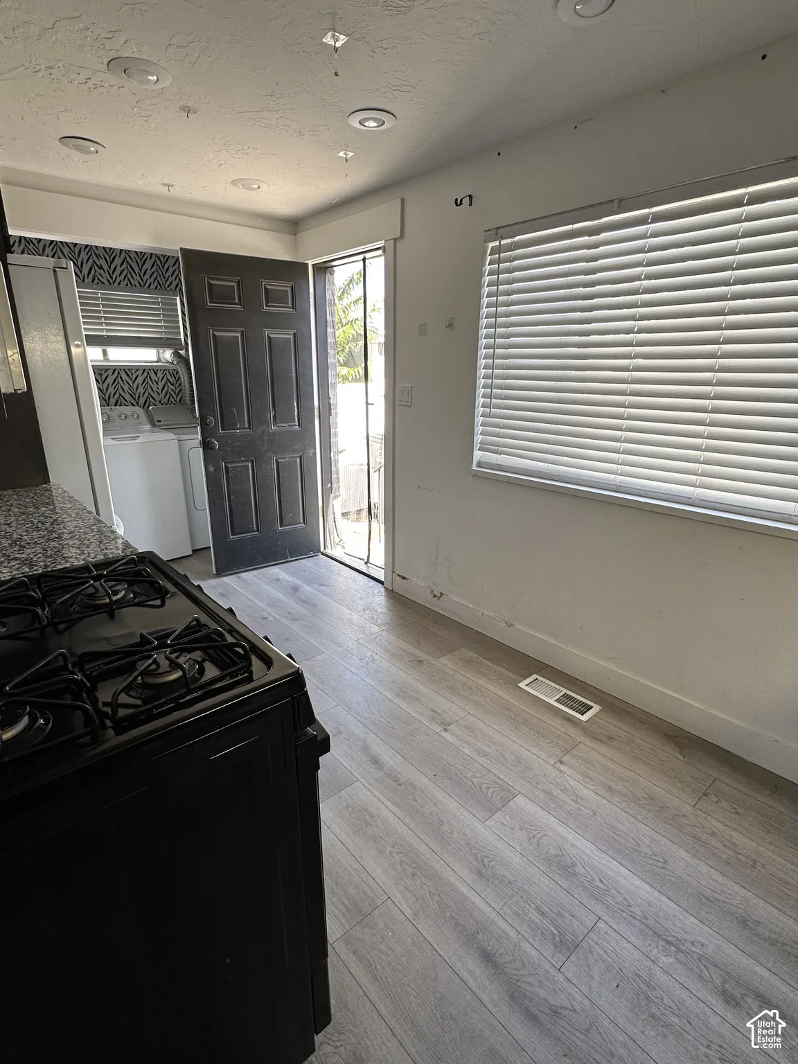 Wood-finish flooring with a gas range, recessed ceiling lights, a tiled backsplash, and a large window with blinds