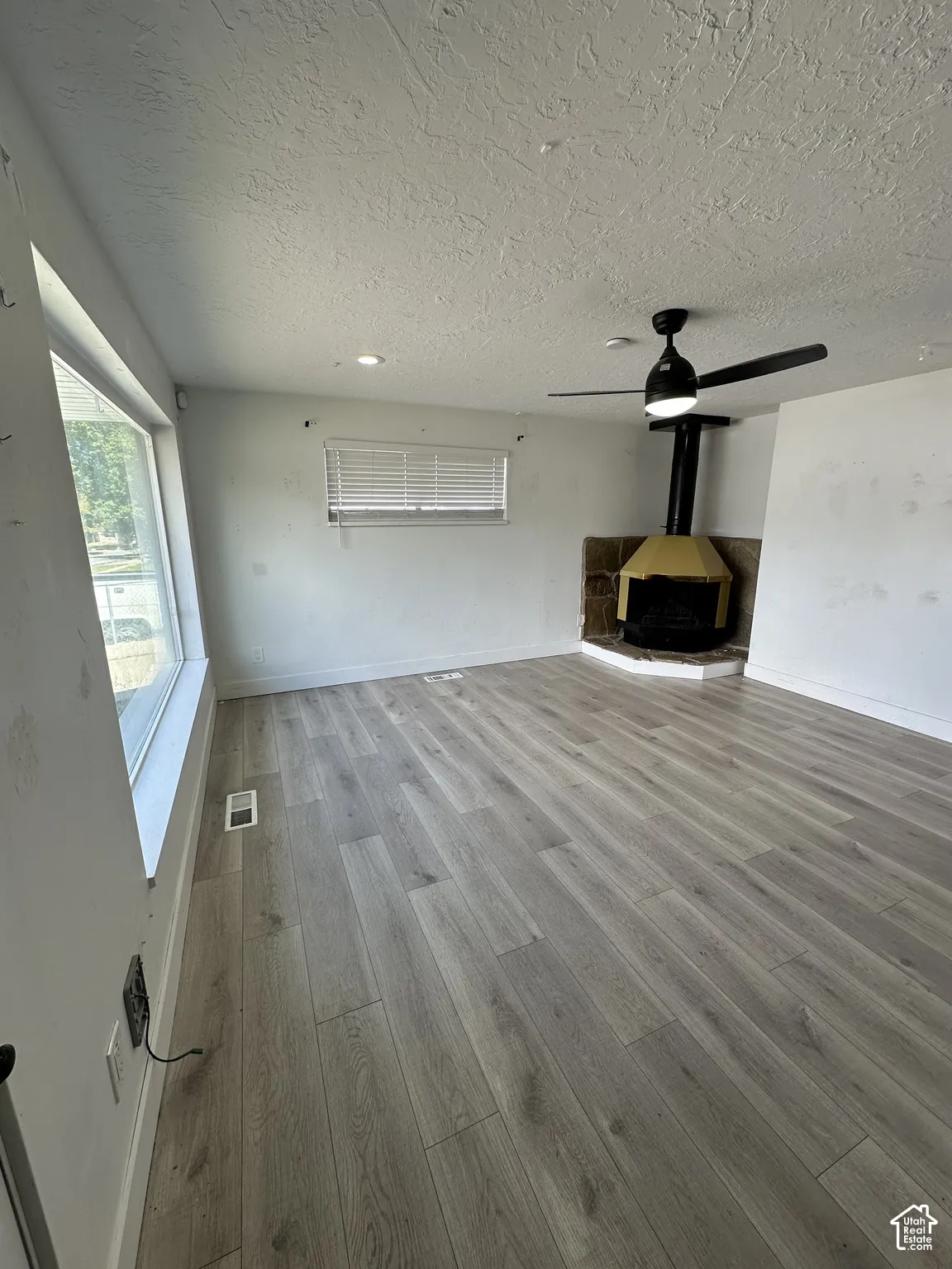 Wood-finish flooring, corner fireplace with stone surround, recessed lighting, ceiling fan, and window with blinds