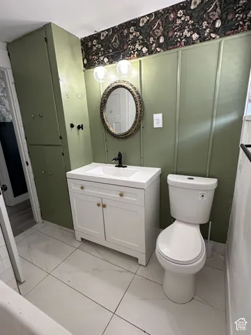 White tile flooring, white vanity with integrated sink, black finish faucet, ornate framed mirror, and built-in storage cabinetry