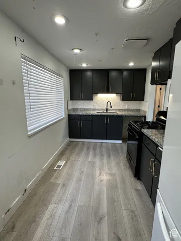 Recessed lighting illuminates the kitchen, featuring wood-finish flooring, dark cabinetry, and stone-finish countertops