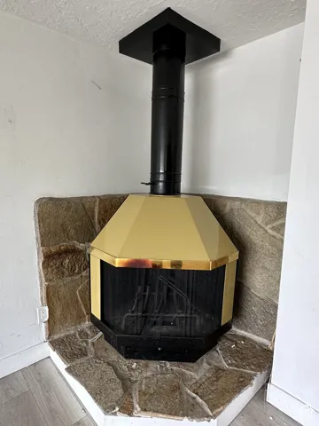 Freestanding corner fireplace with a gold-toned hood, black flue, and stone hearth