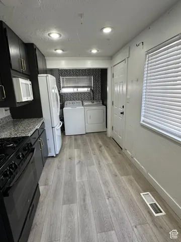 Kitchen featuring wood-finish flooring, recessed lighting, black cabinetry with gold-tone hardware, and a granite-patterned countertop
