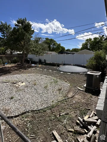 Expansive backyard featuring a gravel-covered area, mature trees, and a white privacy fence