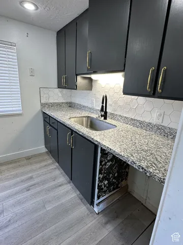 Kitchen featuring dark cabinetry with gold-toned hardware, speckled countertops, a hexagon tile backsplash, and a stainless steel sink with a black faucet