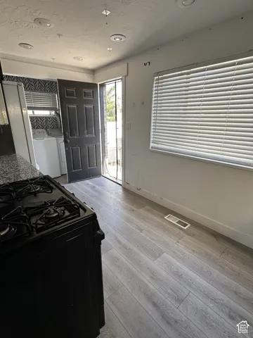 Wood-finish flooring with a gas range, recessed ceiling lights, a tiled backsplash, and a large window with blinds
