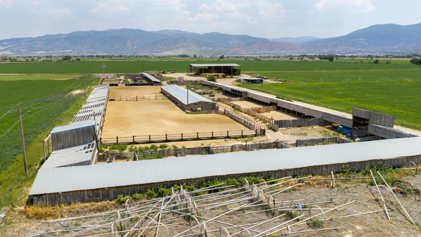 Expansive equestrian facility featuring multiple fenced riding arenas, covered stall structures, and open-air paddocks