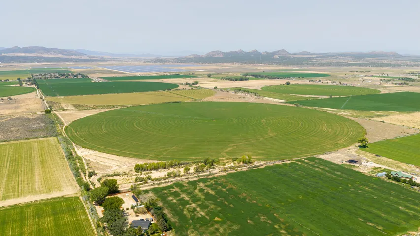 Expansive agricultural land featuring multiple circular crop fields, surrounding green fields, and distant hills