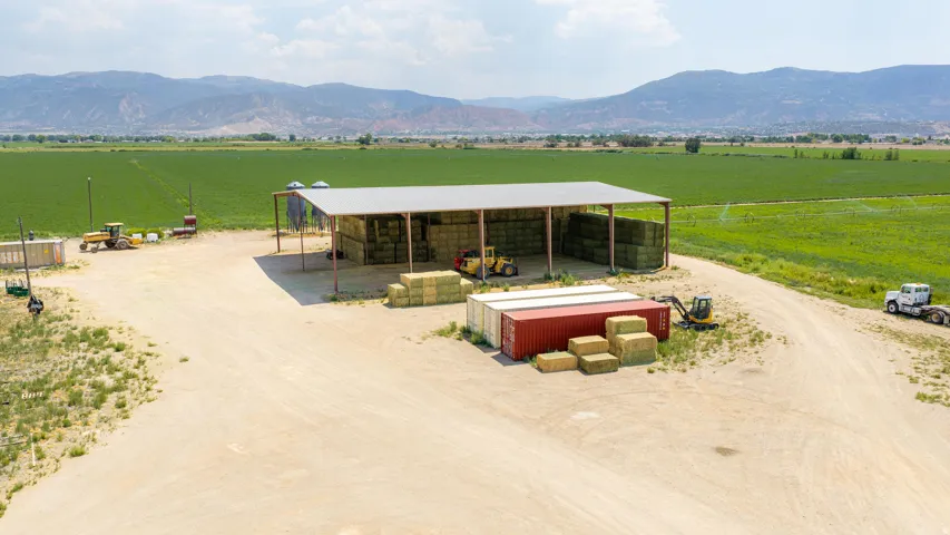 Expansive agricultural property featuring a large open-sided barn with a metal roof, two silos, and a wide dirt drive