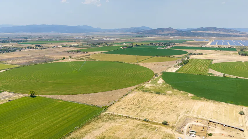 Expansive agricultural land featuring circular fields, linear crop rows, and distant mountain ranges