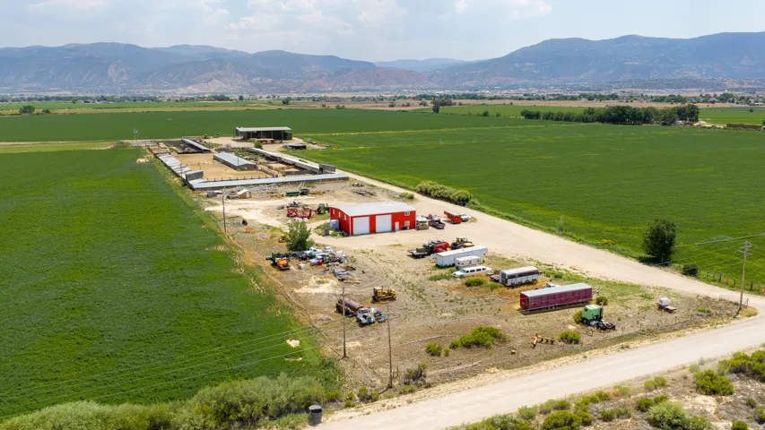 Expansive agricultural property featuring a red metal building, multiple outbuildings, and a large cultivated field