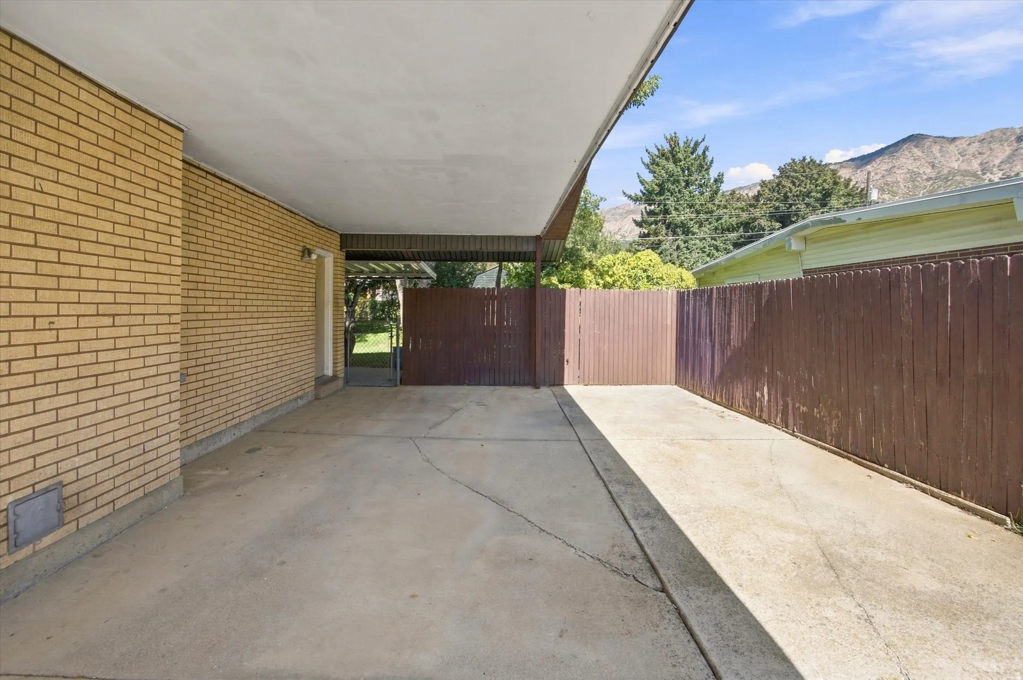 Covered carport with a concrete slab, brick exterior, wood privacy fence, and mountain backdrop